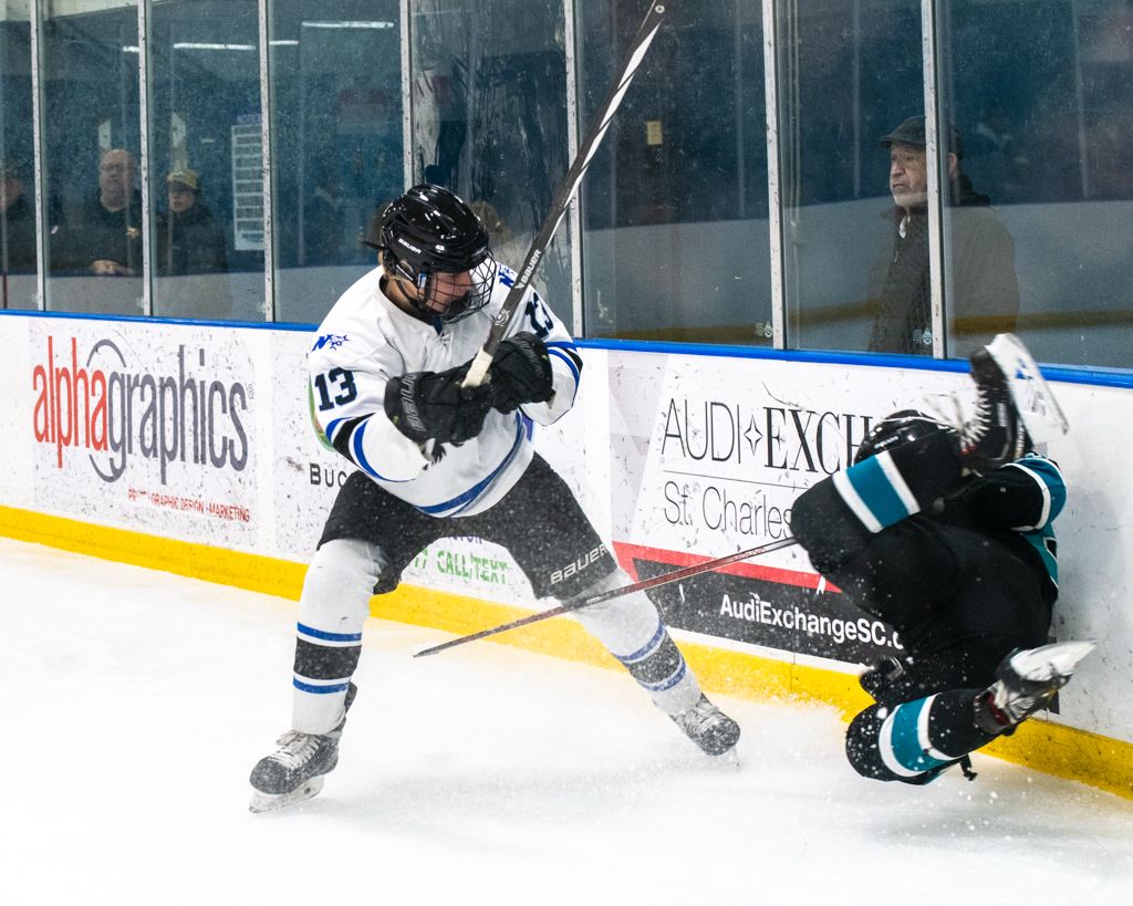 Hockey players chase after the puck along the boards during a competitive match.