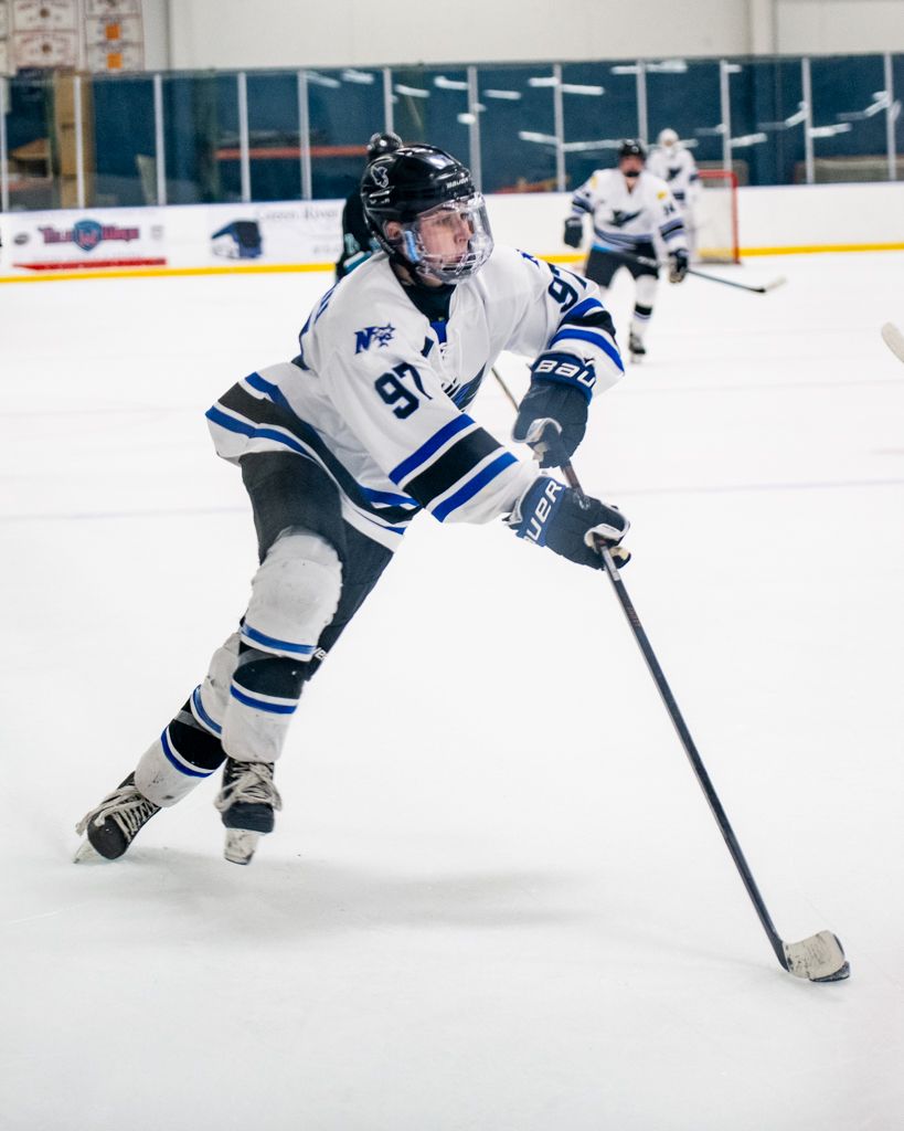 Hockey player in white jersey controlling puck while skating on ice rink.