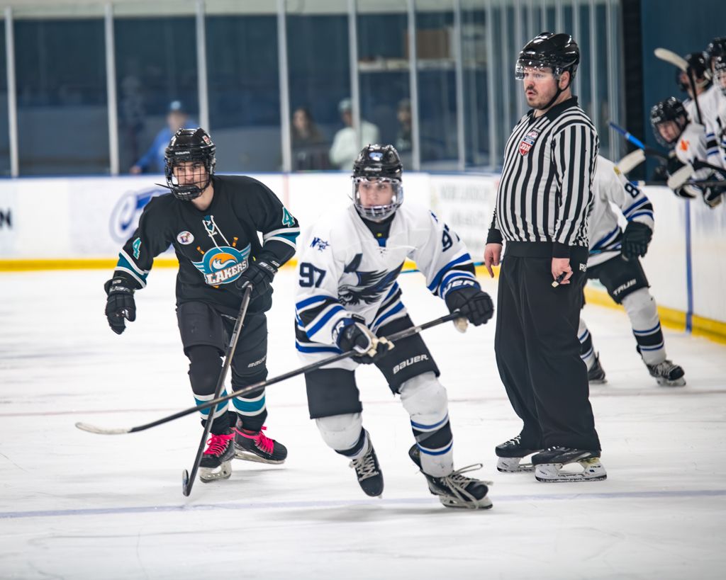 Hockey game action shot with players skating and referee on ice rink.