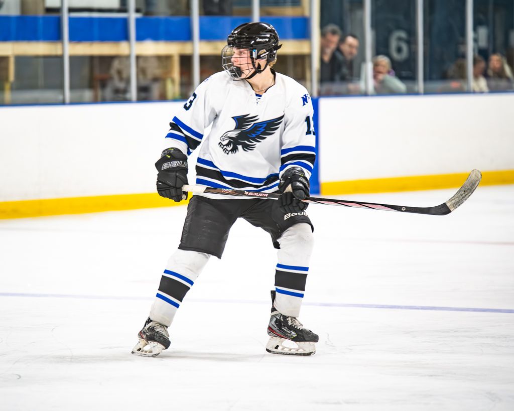 Hockey players in white and blue jerseys skating during a competitive match.