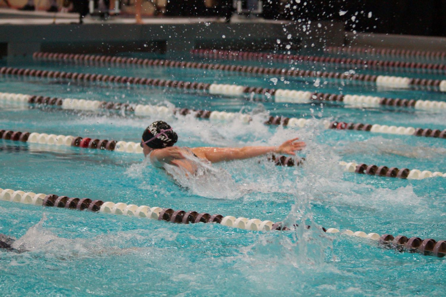 Competitive swimmer racing in freestyle stroke through pool lane with water spraying.