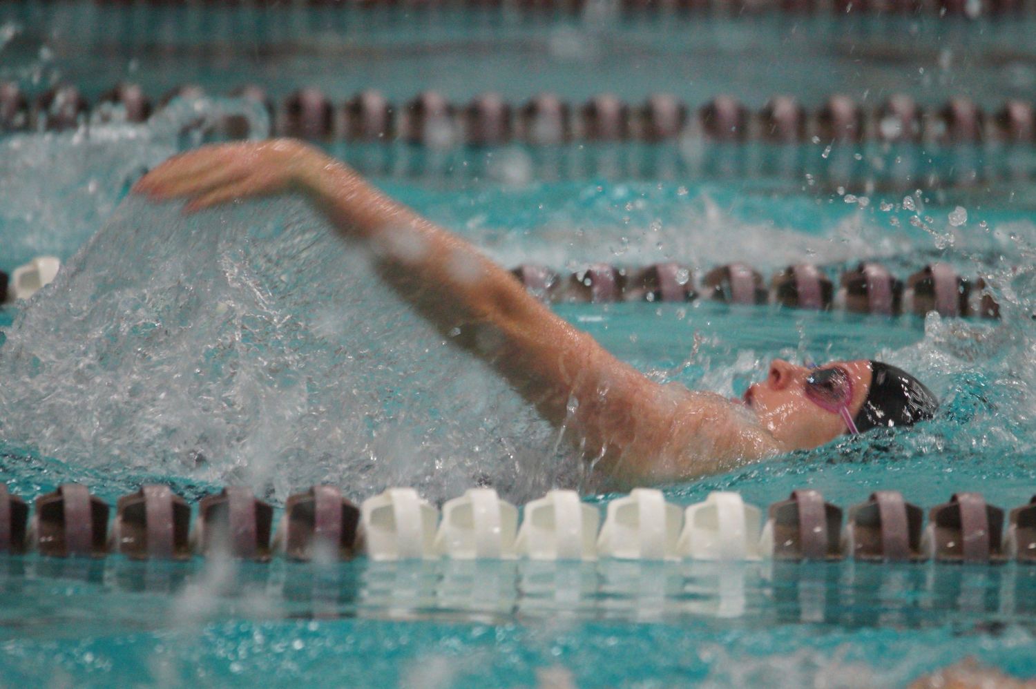 Swimmer performing freestyle stroke in competitive pool lane with splashing water.