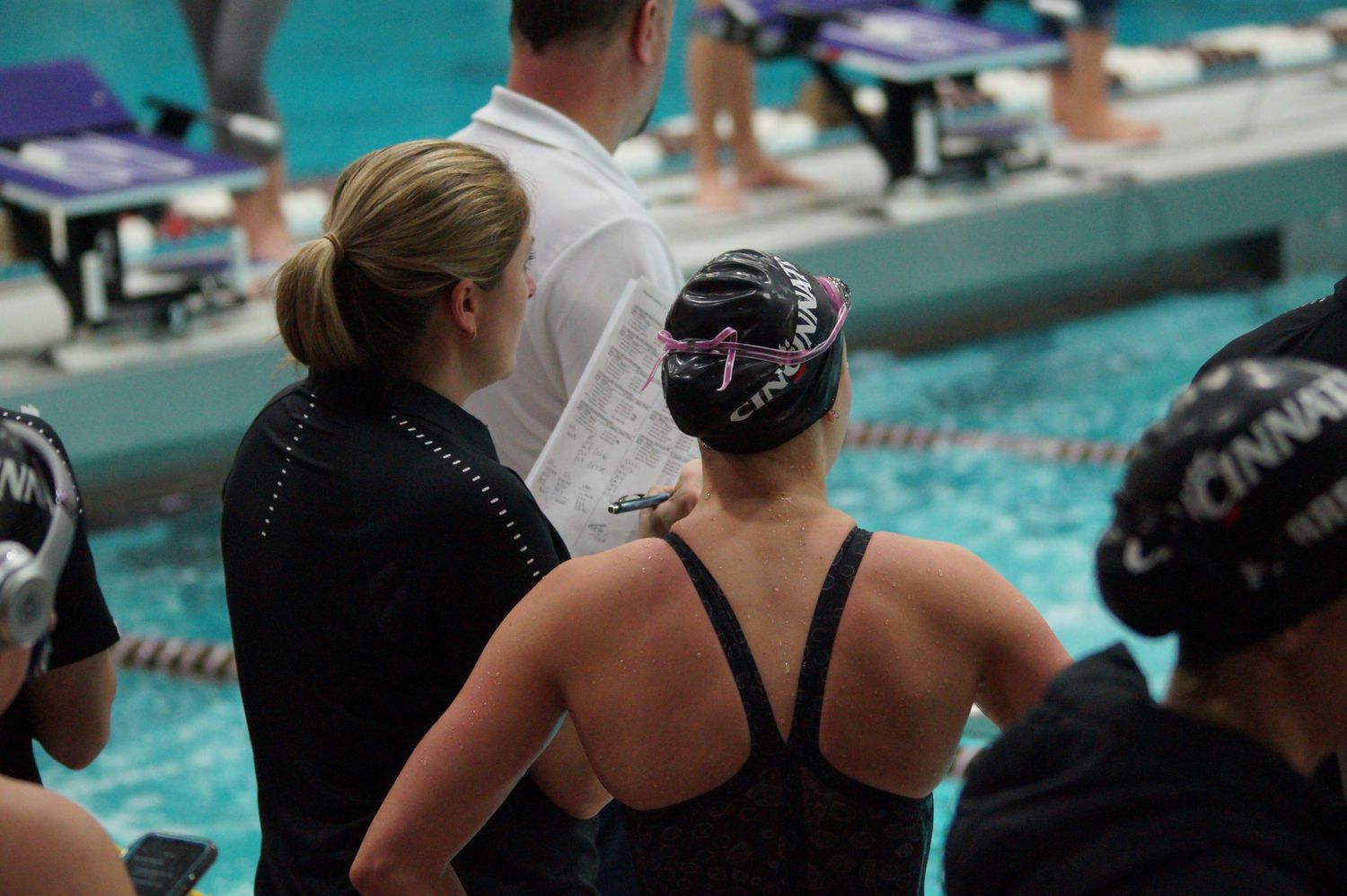 Swimmers and coaches gathering poolside during competitive swimming meet.