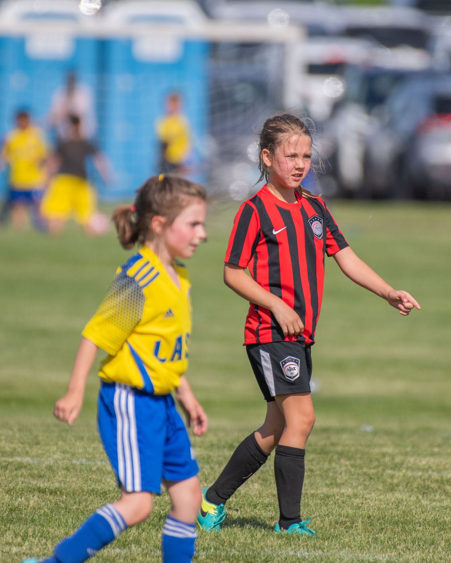 Youth soccer players in red and blue uniforms compete for ball on grass field.