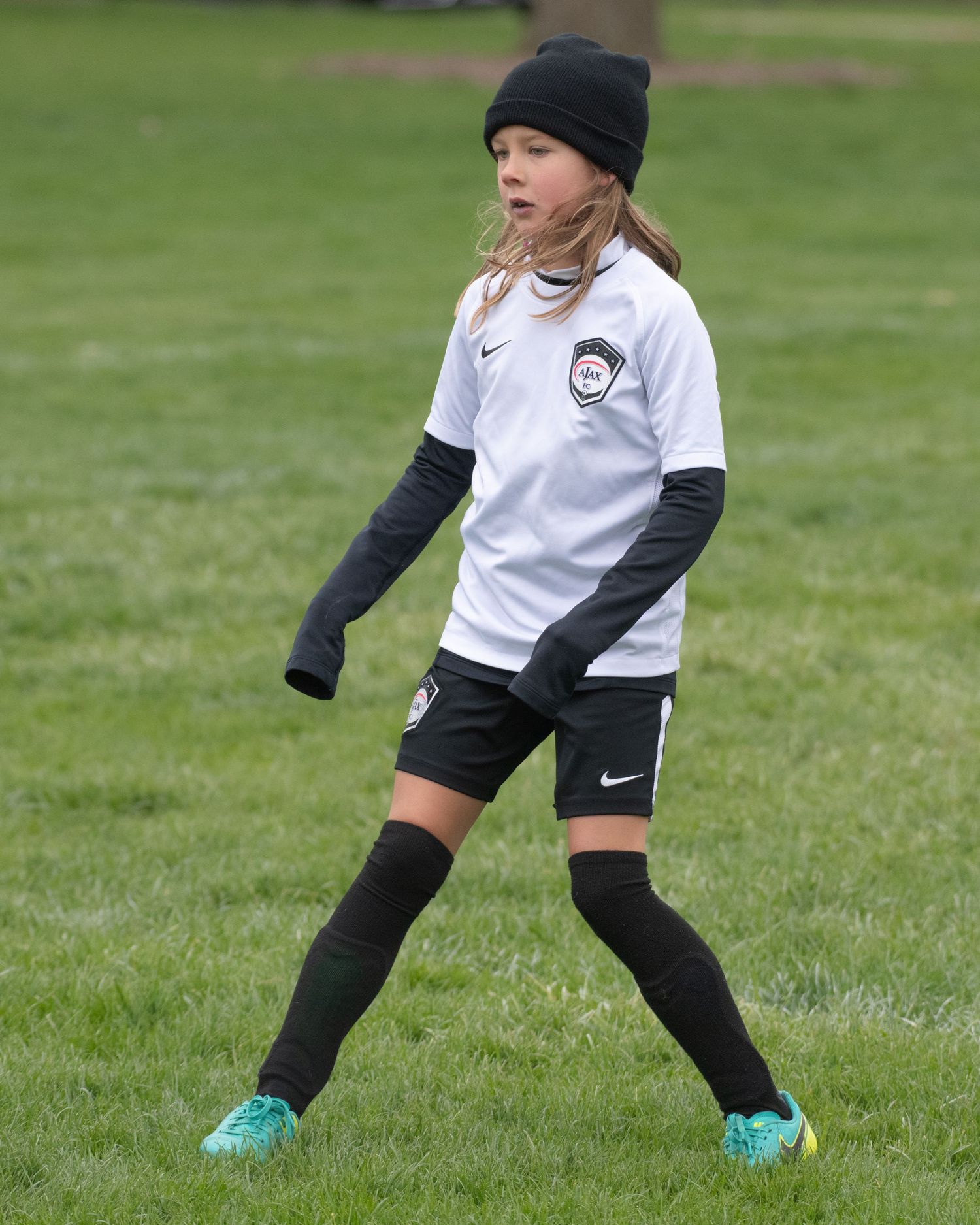 Young soccer player in black winter hat and white jersey practices footwork drills.