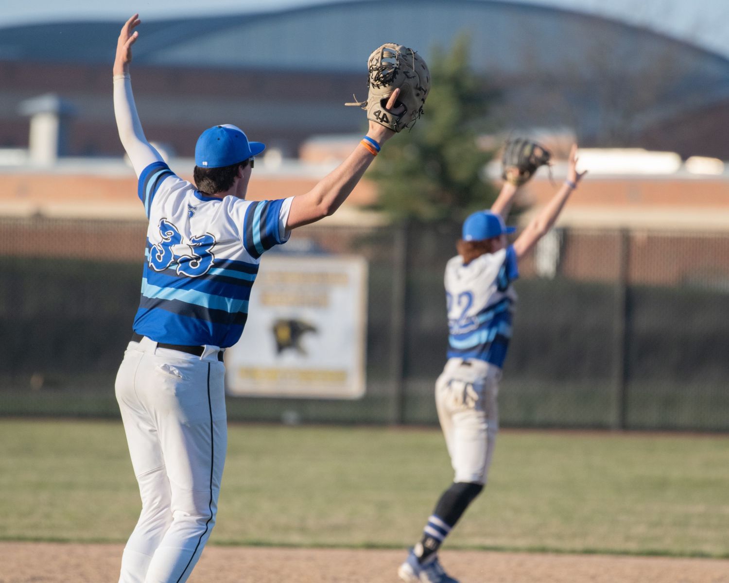 Baseball players in blue uniforms stretching arms up during practice.