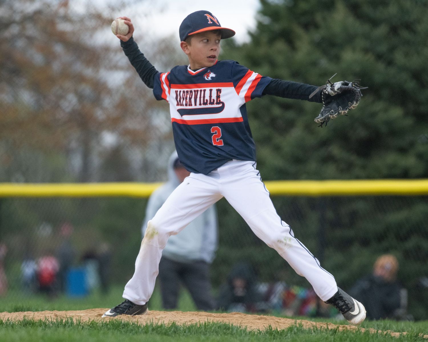 Youth baseball player winds up to throw pitch on dirt mound.