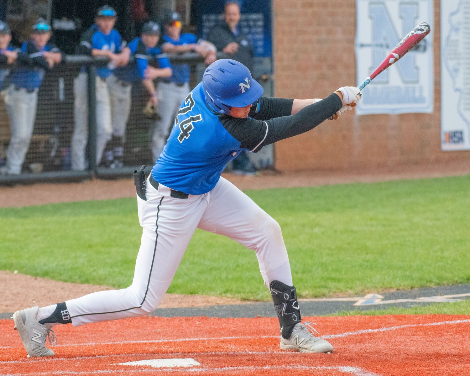 Baseball batter in blue uniform swinging bat at home plate.