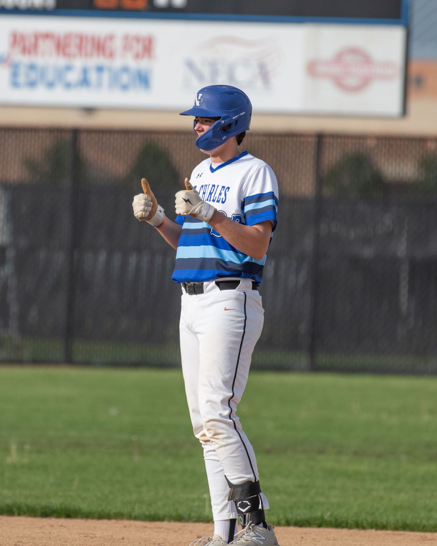 Baseball player in blue and white uniform stands on base giving thumbs up signal during game.