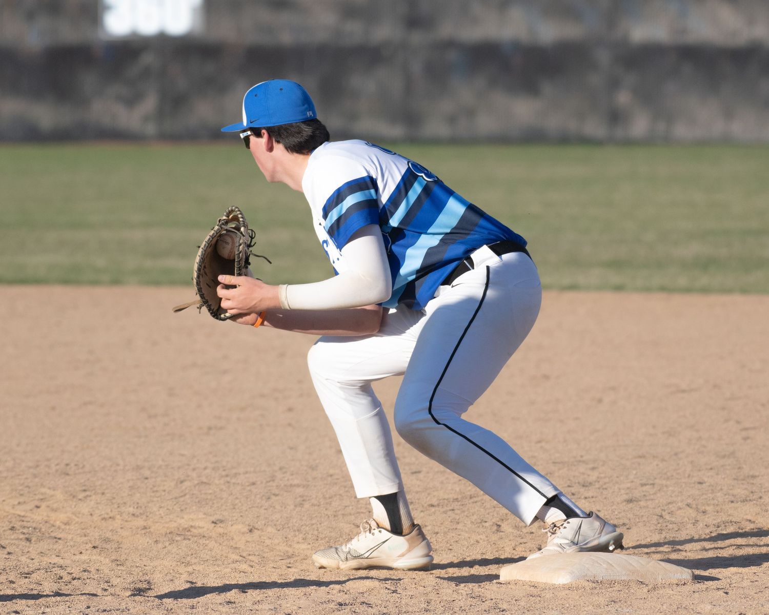 Baseball player in blue and white uniform ready in fielding position.