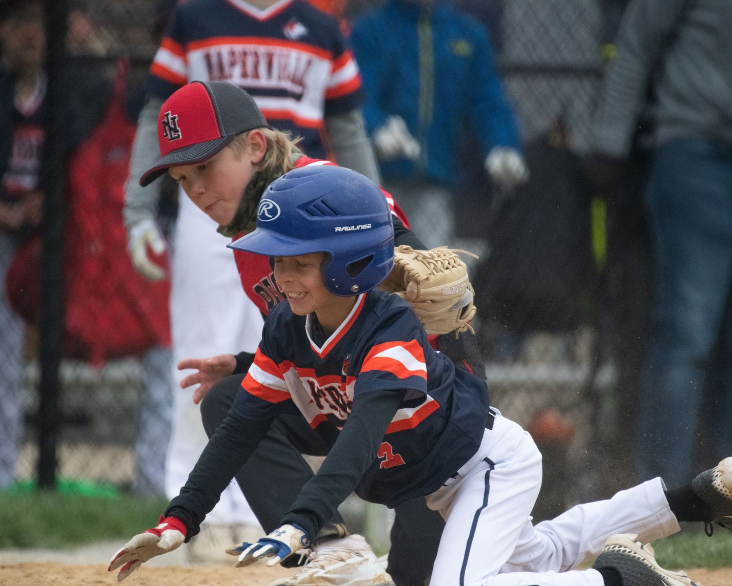 Baseball players sliding and tagging base during competitive youth game.