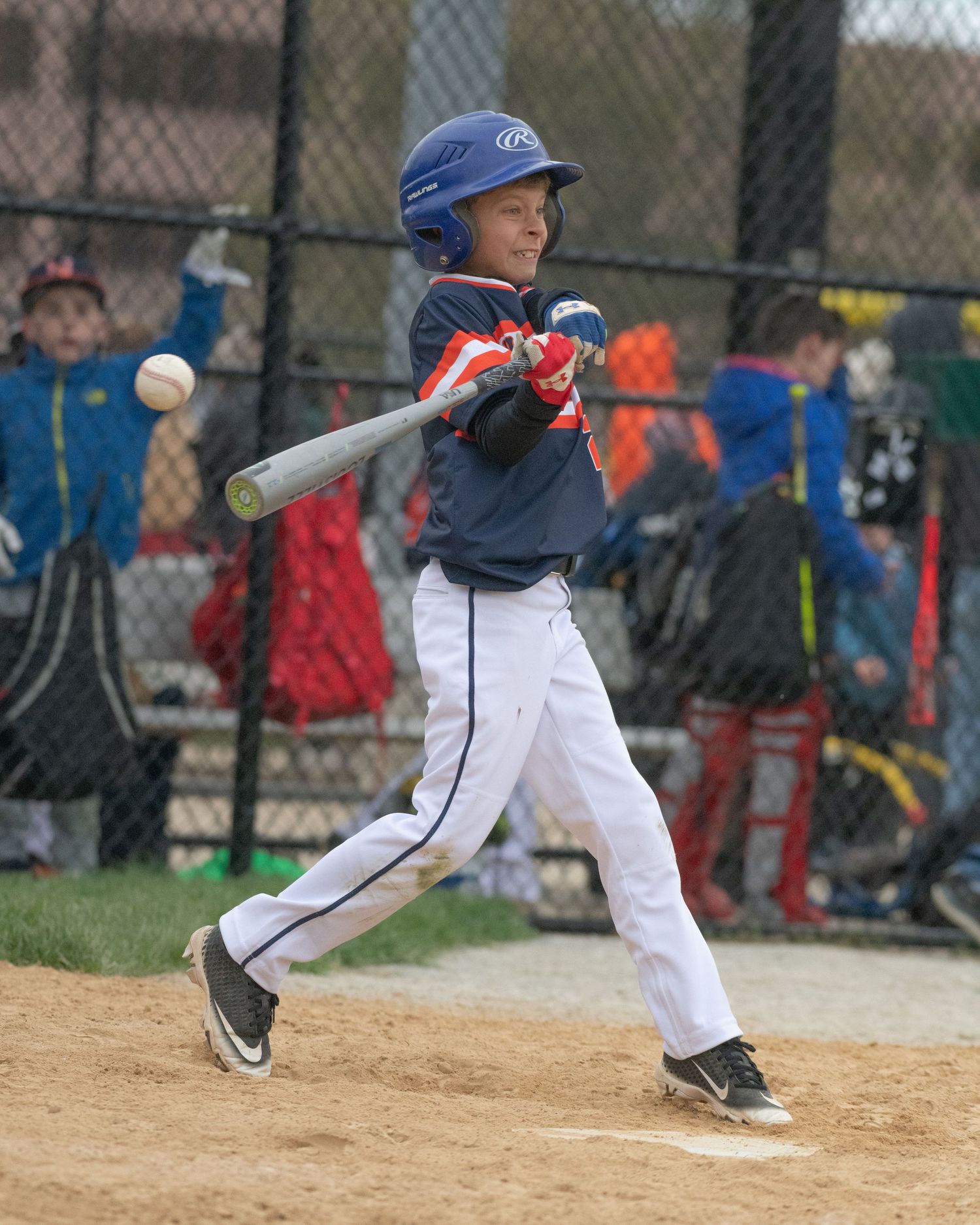 Baseball player in blue helmet swings bat during youth league game.