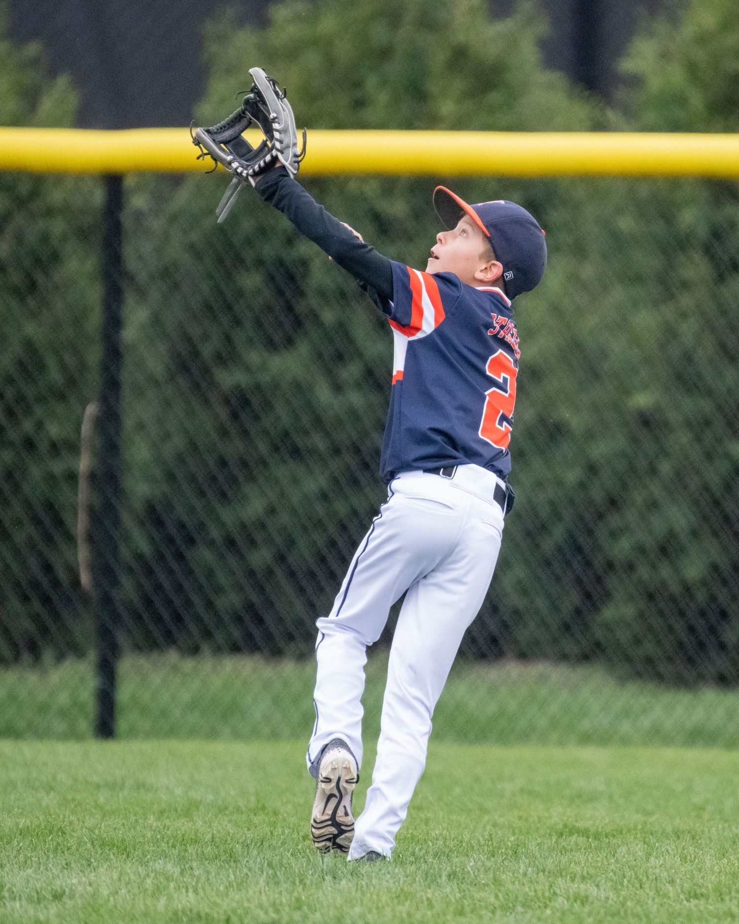 Young baseball player looks up at ball against yellow foul pole during batting practice.