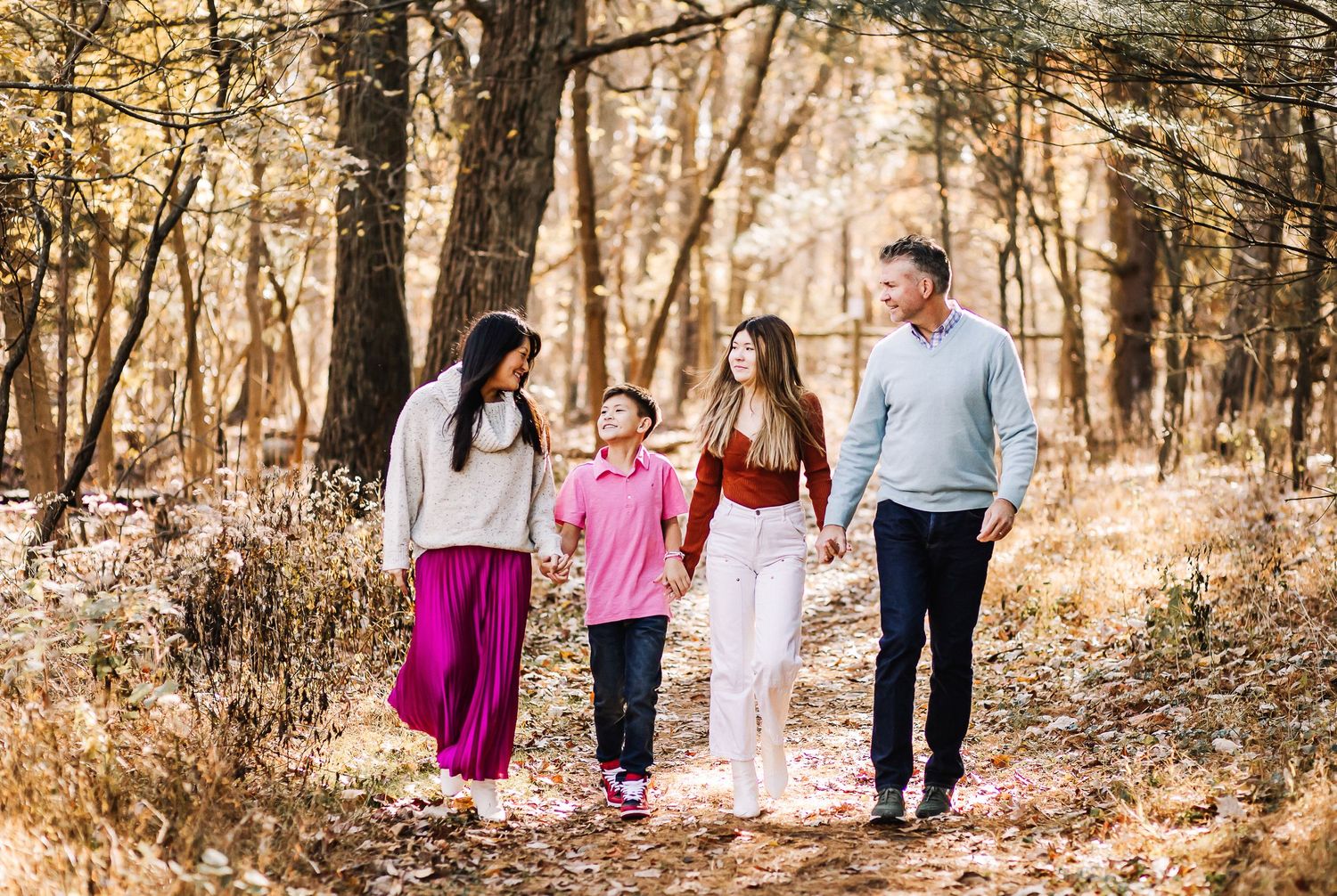 Family of four walking together on a scenic autumn trail through the woods.