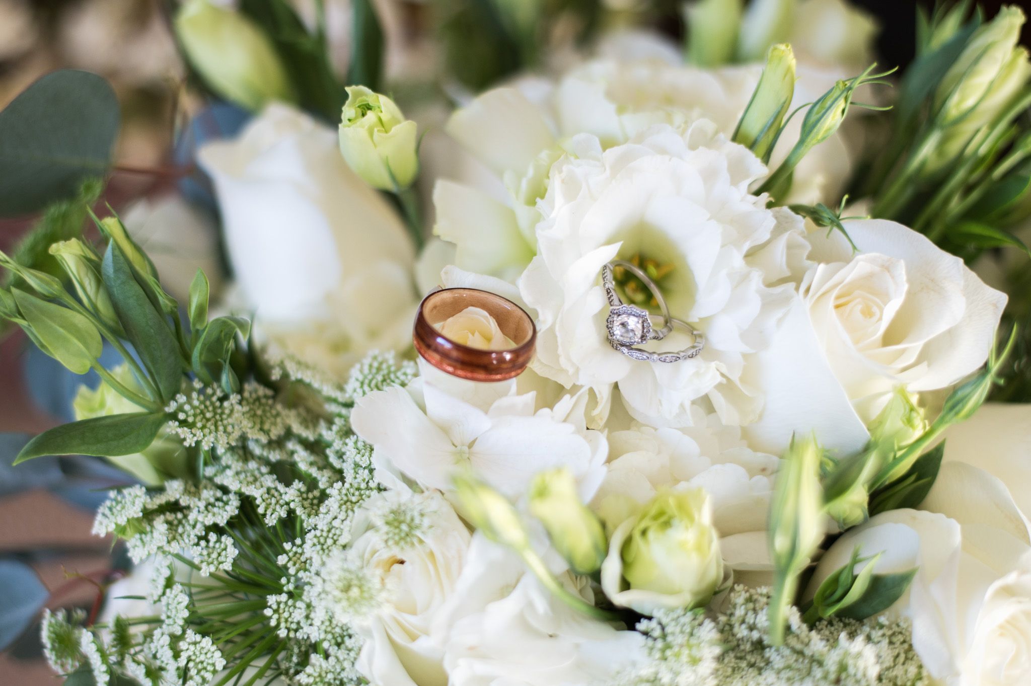 White wedding rings nestled among delicate white roses and greenery in a bridal bouquet.