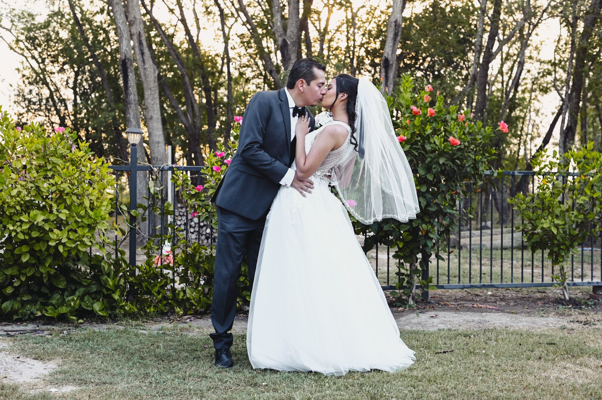Romantic wedding moment captured in a garden setting with iron fence and greenery backdrop.