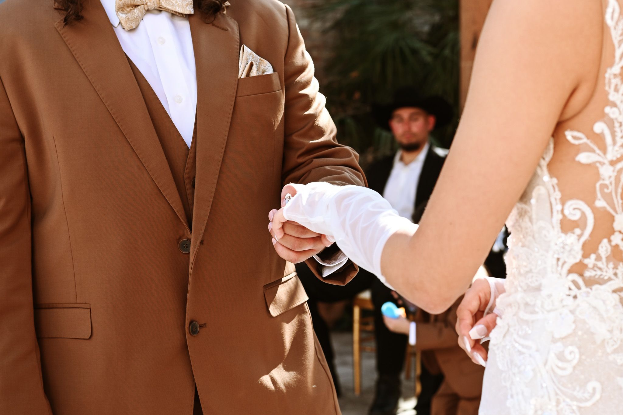 Close-up of hands holding during a wedding ceremony with a groom in a brown suit.