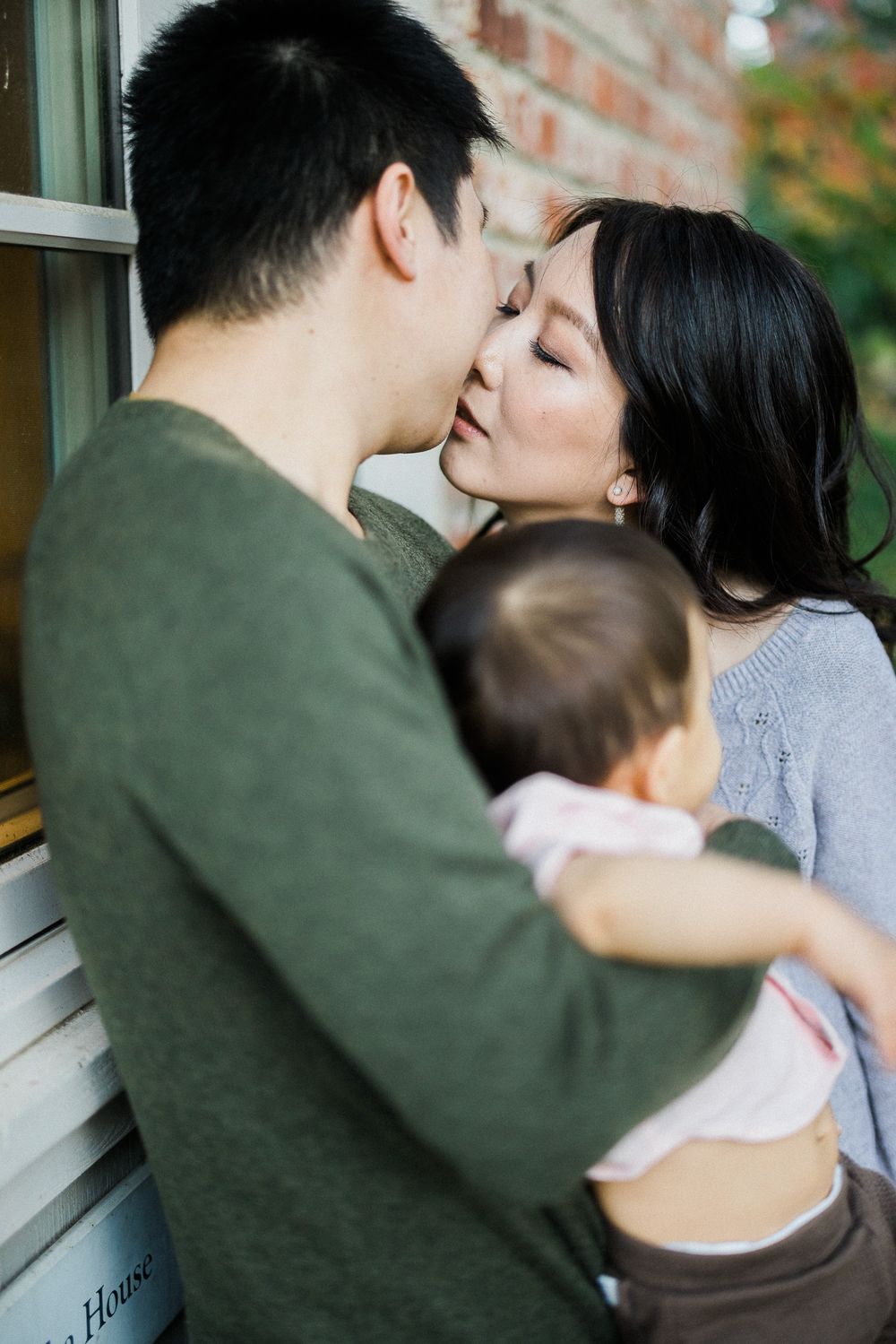 Intimate family embrace captured against a brick wall background.