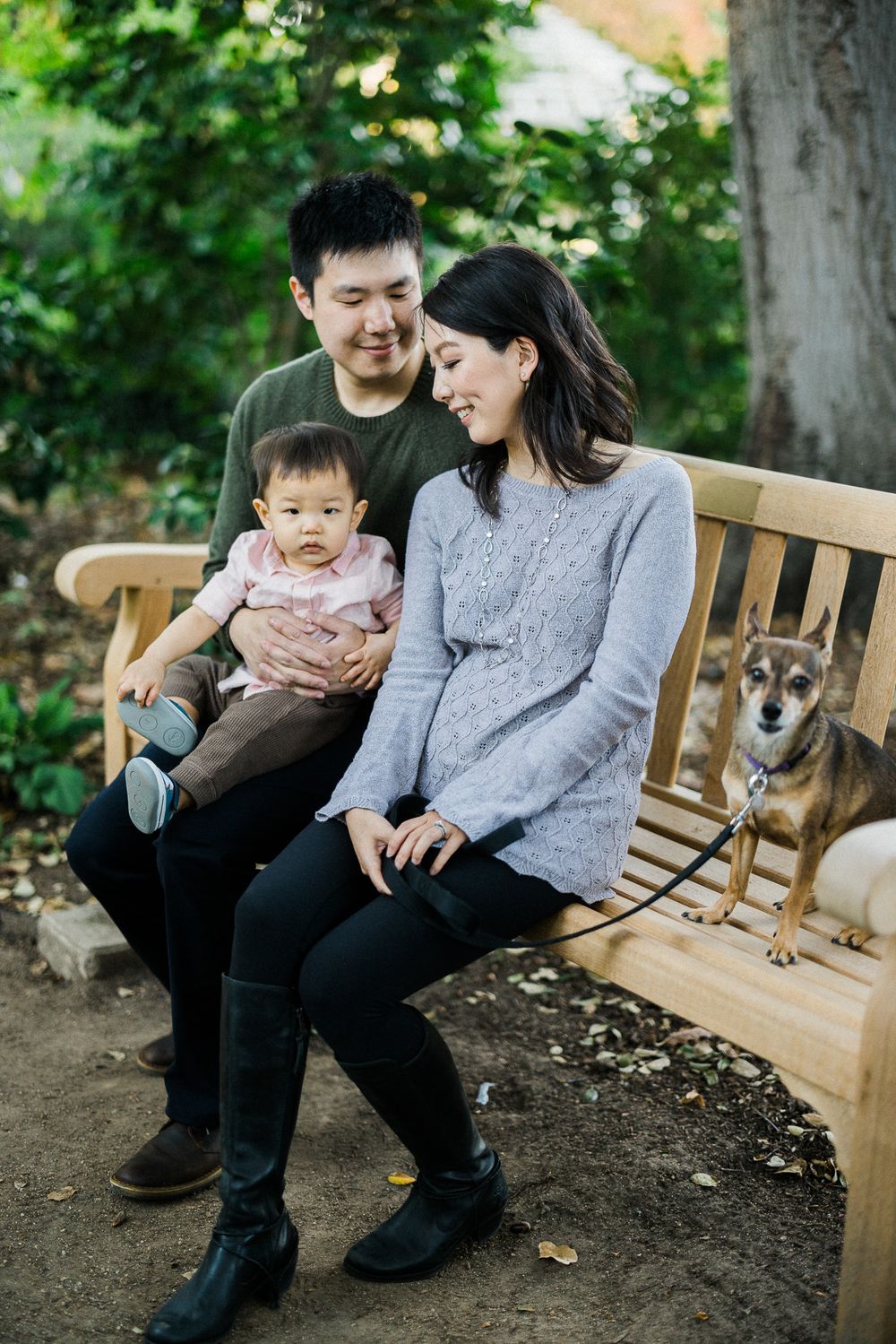Family sitting on wooden bench with their dog in garden setting.