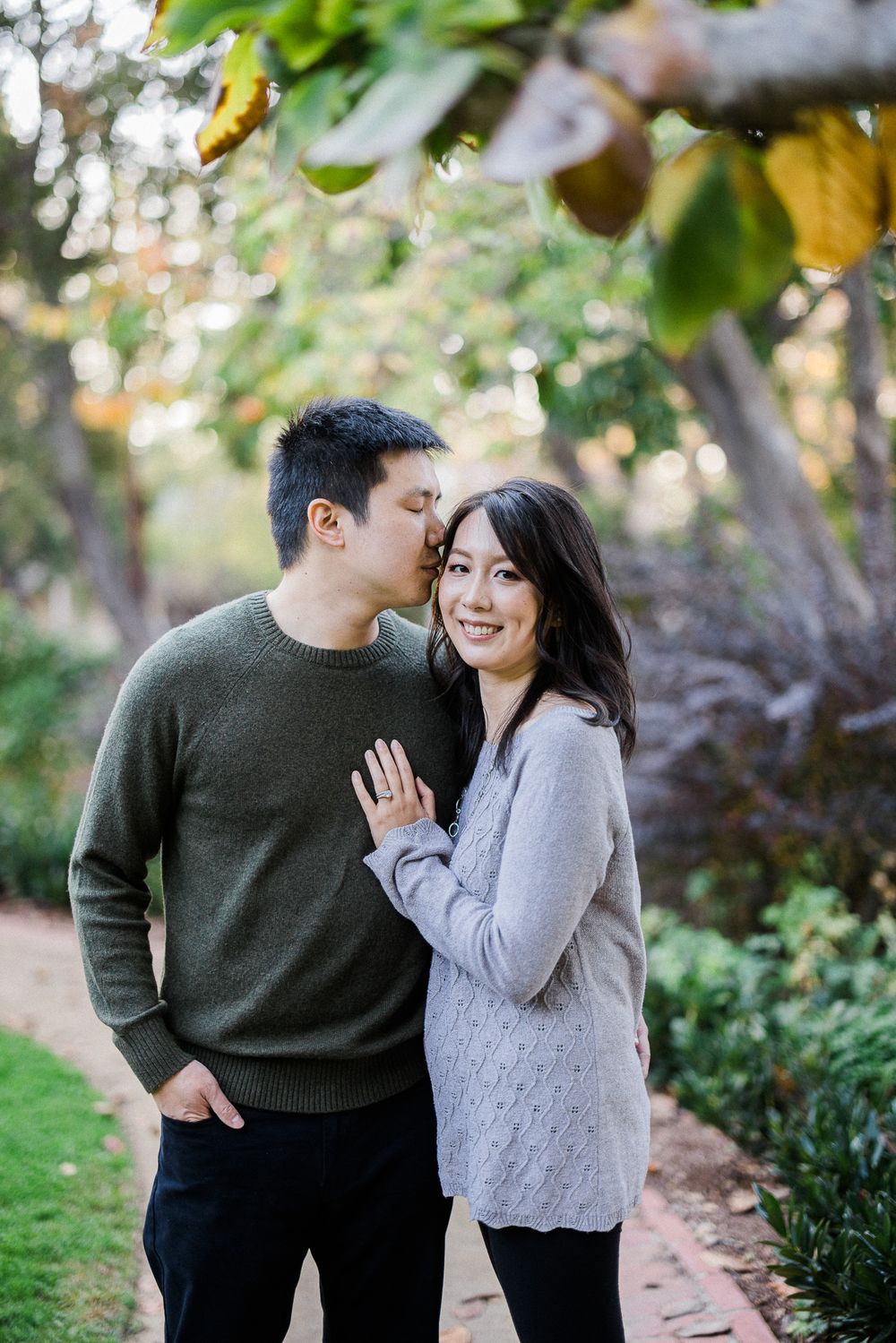 Romantic couple embracing on garden path during golden hour with trees in background.