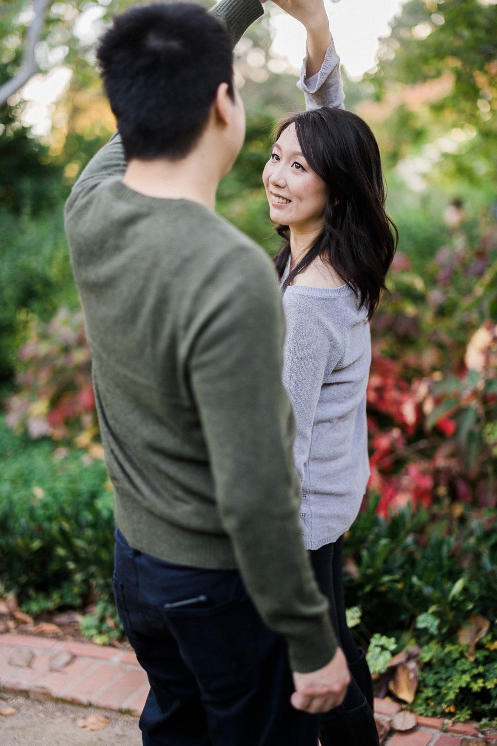 Couple shares a playful moment together on a garden path surrounded by autumn foliage.