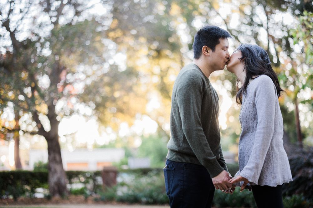 Intimate moment between couple standing on path with sunset light filtering through trees.