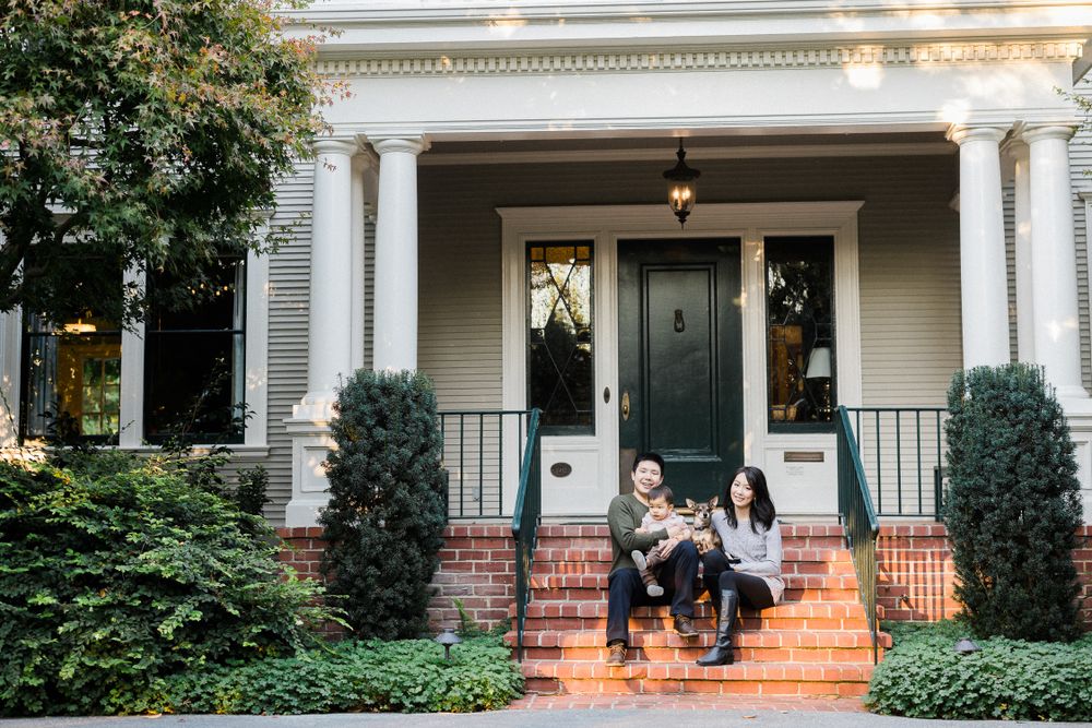 Family sitting on brick steps of classic colonial-style home with white columns and black door.