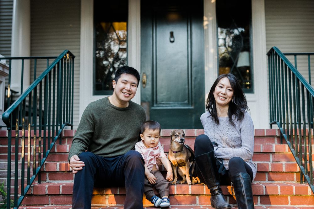 Happy family with baby and dog sitting on front porch steps of historic home.