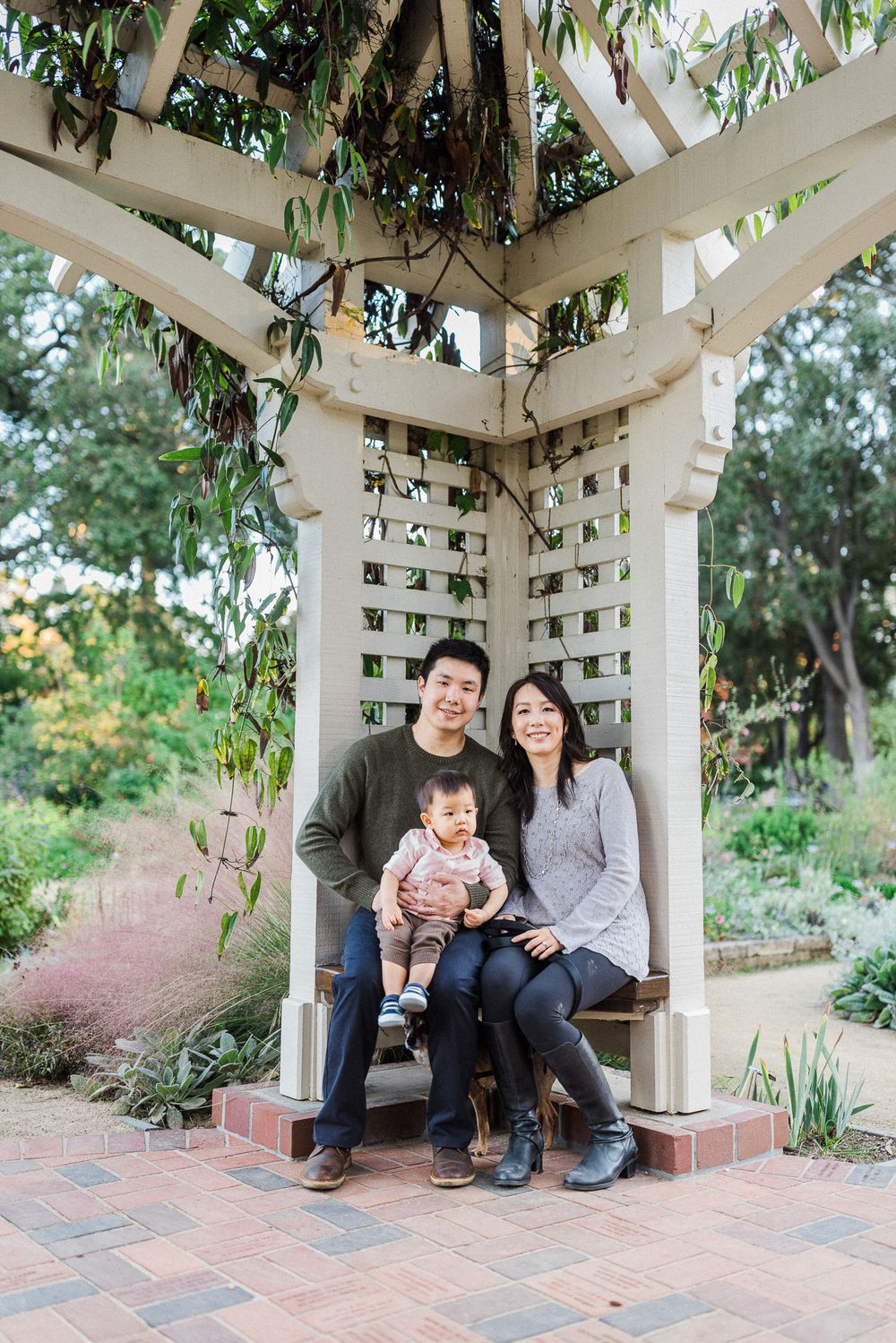 Family portrait under white pergola with climbing vines in garden setting.