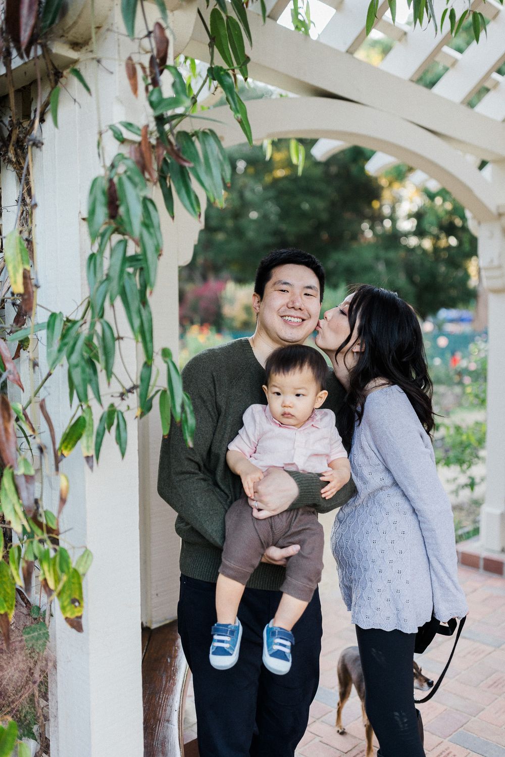 Sweet family moment captured under white garden arbor with eucalyptus leaves.
