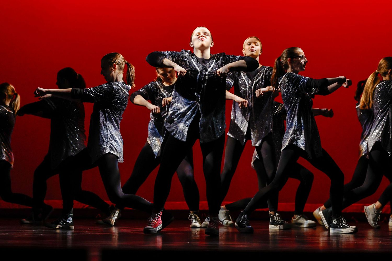 Dancers perform dramatic silhouetted movements against a red backdrop on stage.