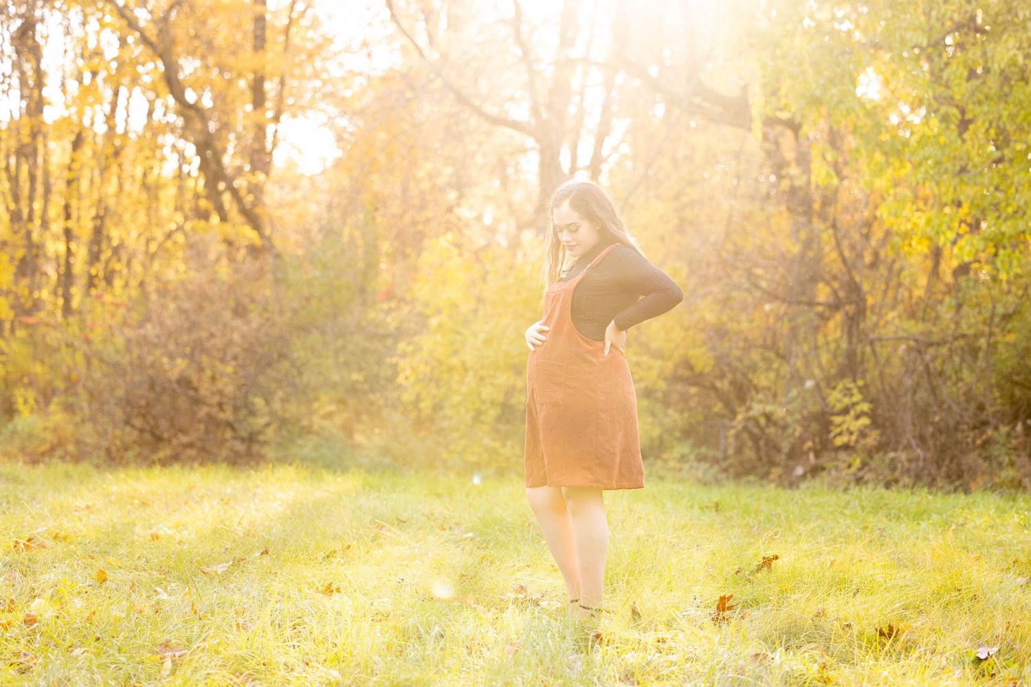 Girl in red jumper holding her stomach during a fall maternity session