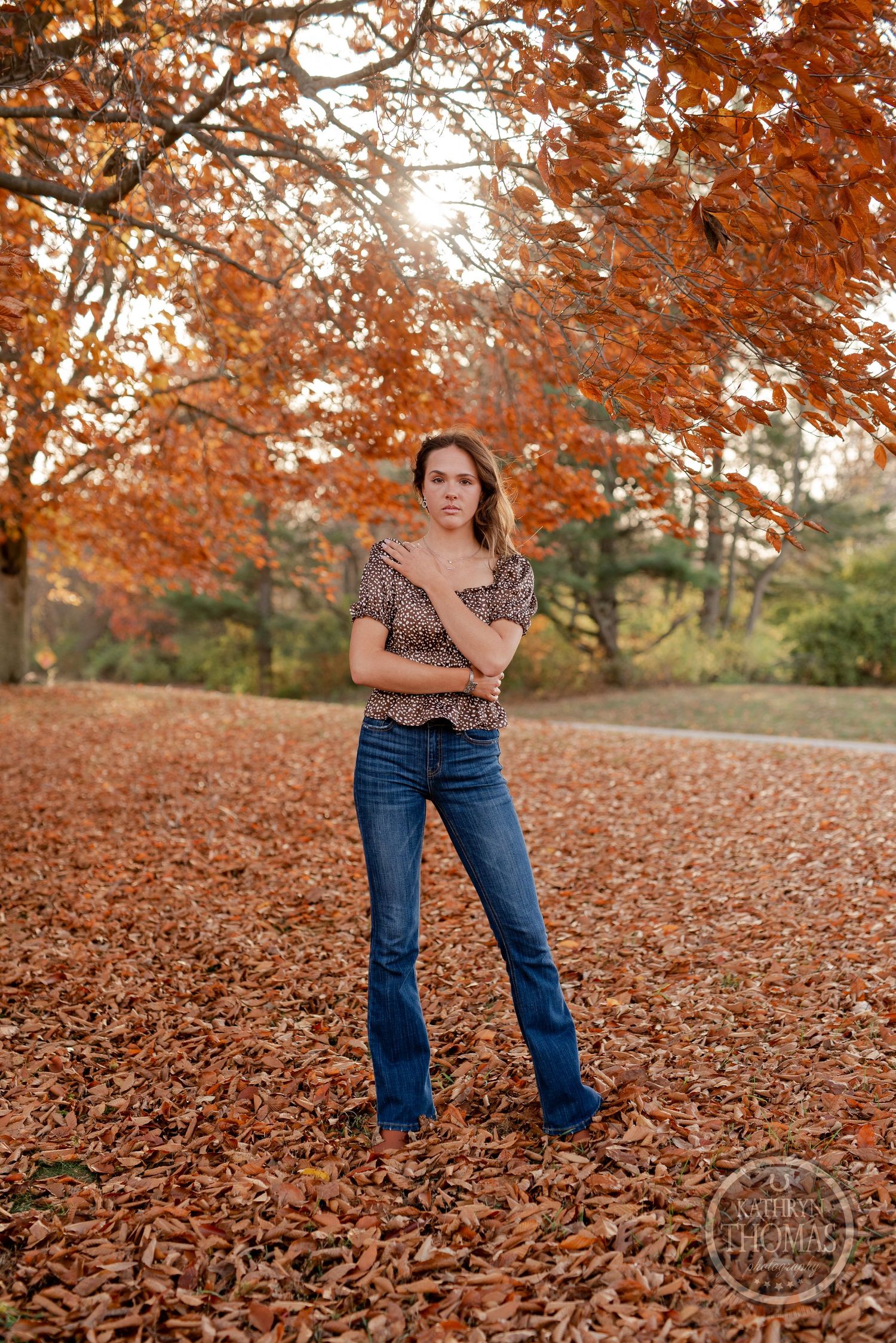Full length portrait standing among autumn leaves wearing patterned top and flared jeans.