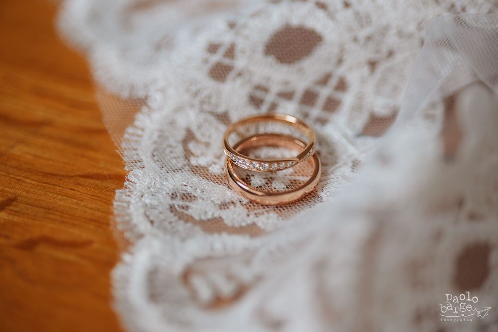 Wedding rings nestled on delicate white lace against wooden surface.