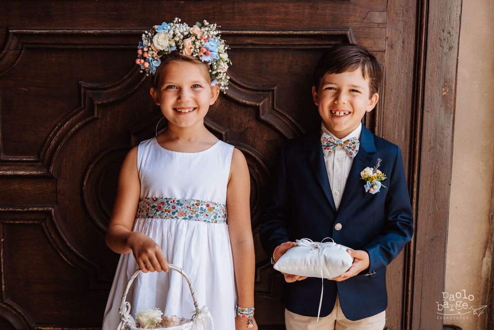 Two young attendants in formal attire pose together before a wooden door.