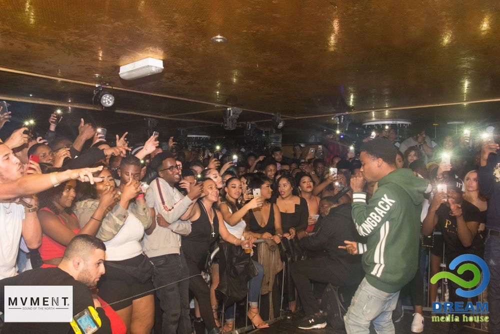 Artist performing on stage engaging with an excited crowd at an indoor nightclub concert.