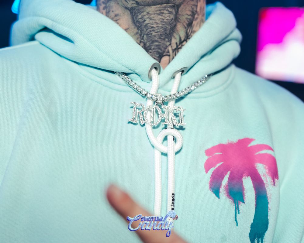 Close-up of a person wearing a mint hoodie with palm tree print and diamond chain necklace.