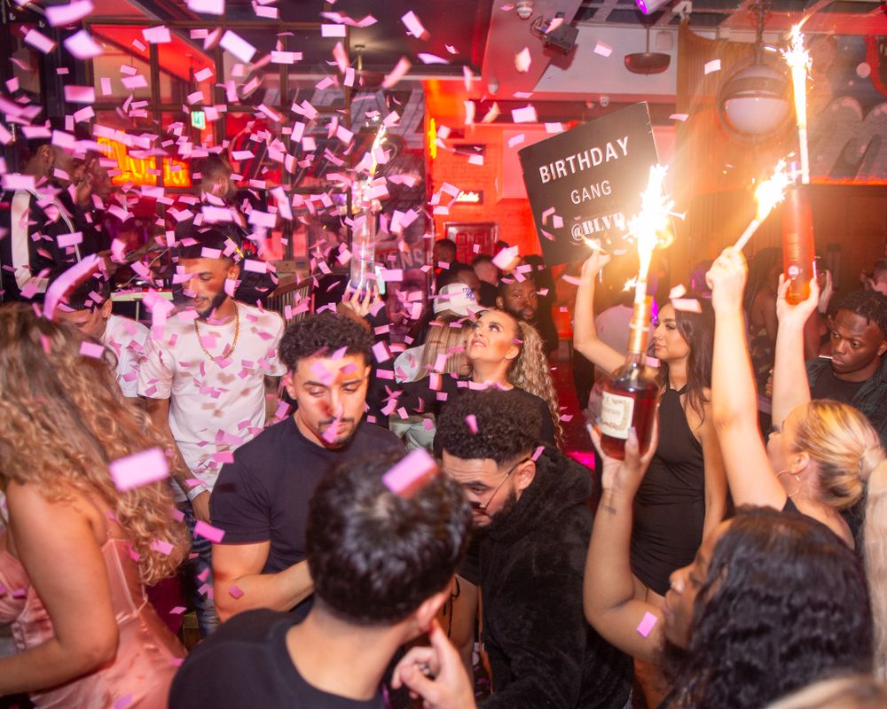 Energetic nightclub birthday party scene with confetti, sparklers and dancing crowd.