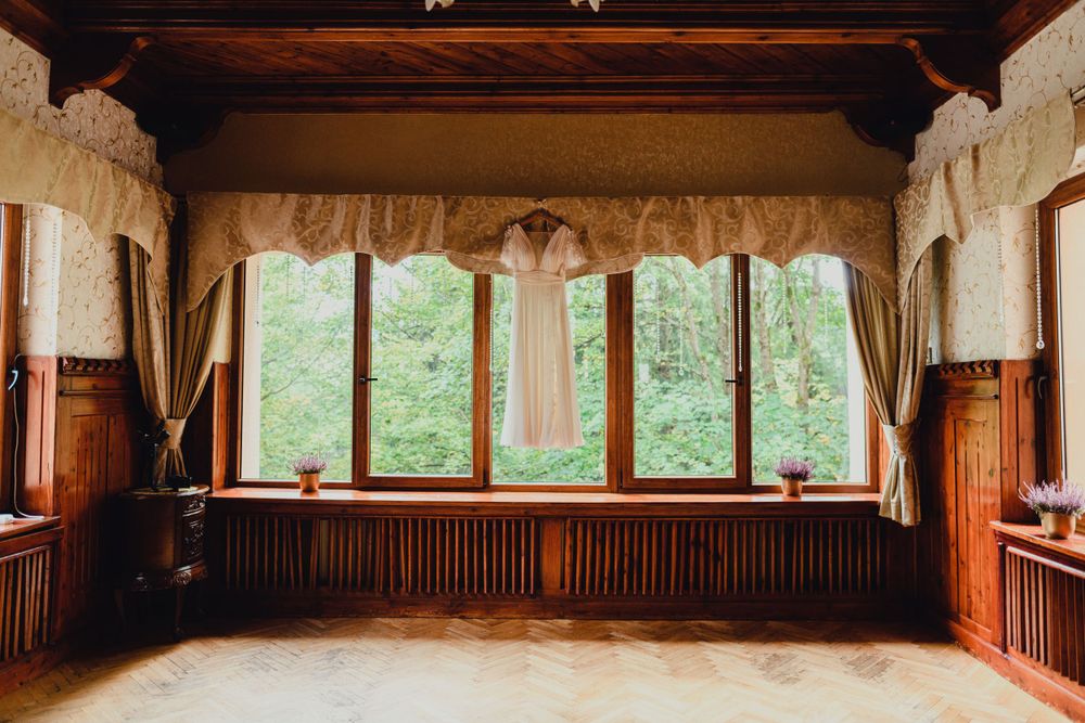 Rustic wooden room with large windows overlooking green forest scenery.