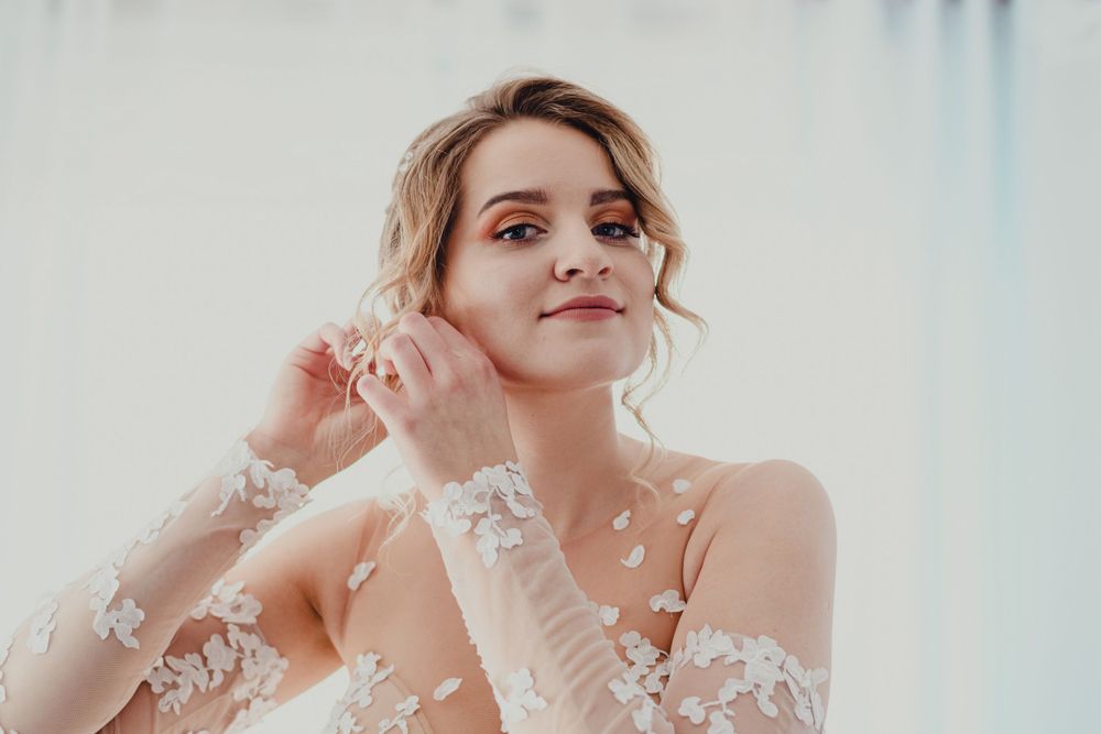 Delicate lace sleeves and soft lighting create an ethereal bridal portrait with romantic styling.