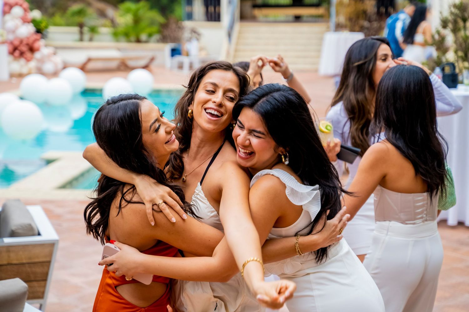 Friends share joyful laughter and hugs during a poolside celebration.