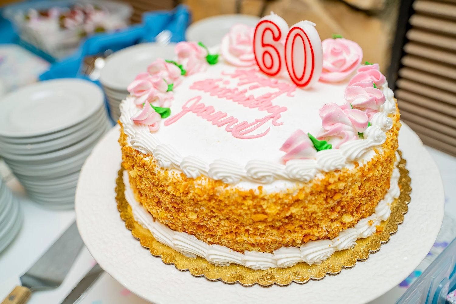 White frosted birthday cake with pink accents and a number 60 candle on top.