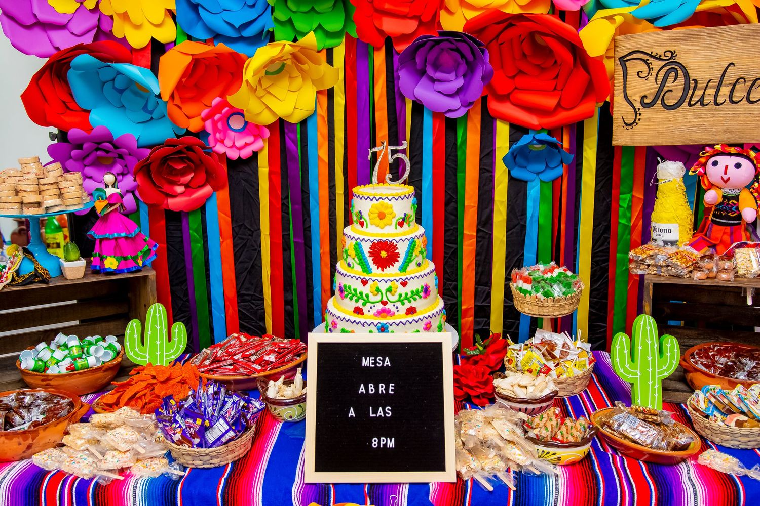Colorful Mexican fiesta dessert table with paper flowers and a decorated cake.