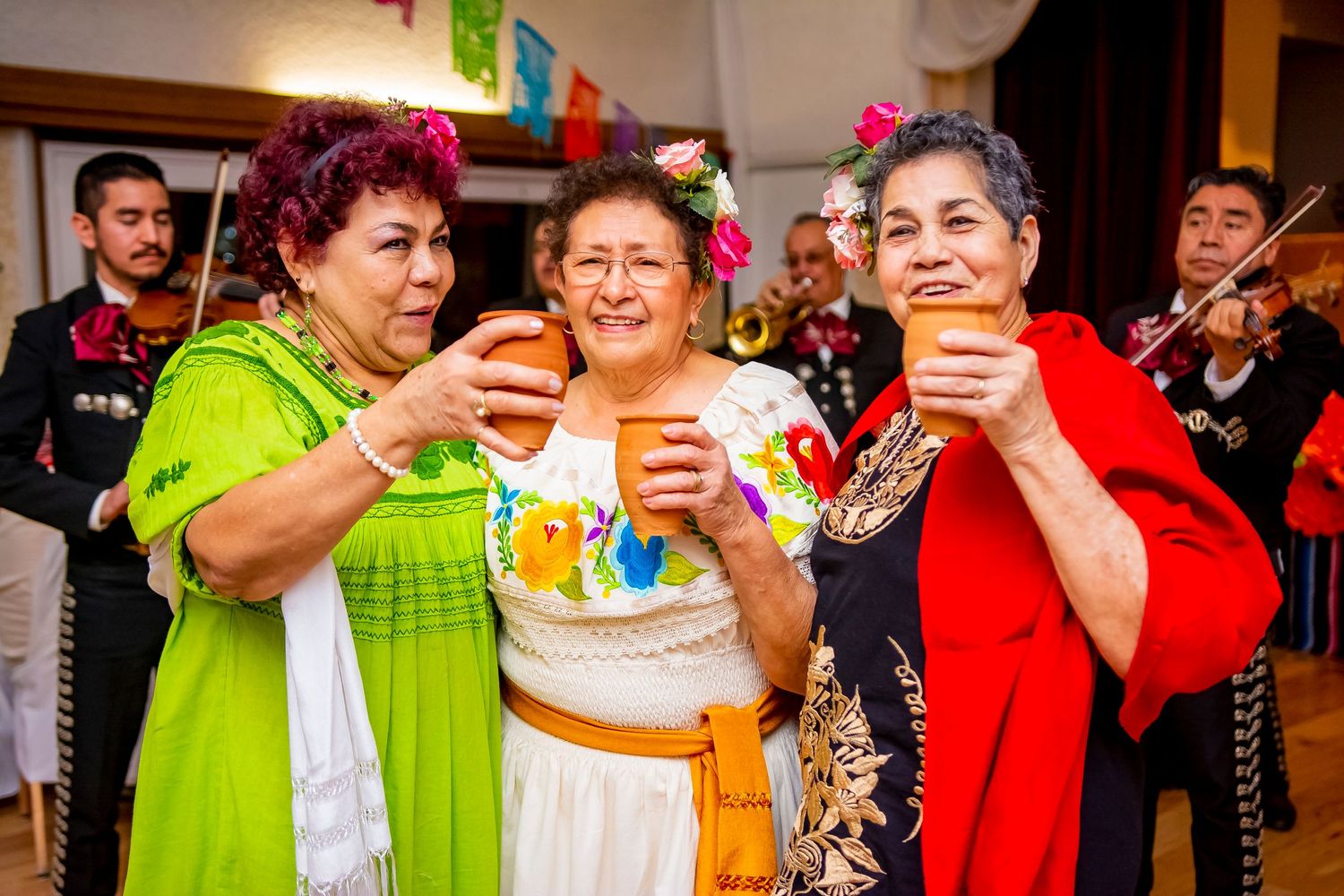 Three people in festive attire toasting with drinks at a celebration.