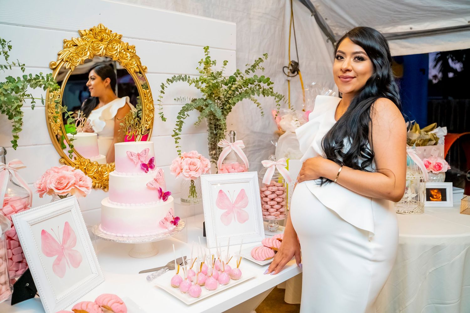 Elegant baby shower dessert table setup with pink decorations, butterfly motifs and a gold ornate mirror.