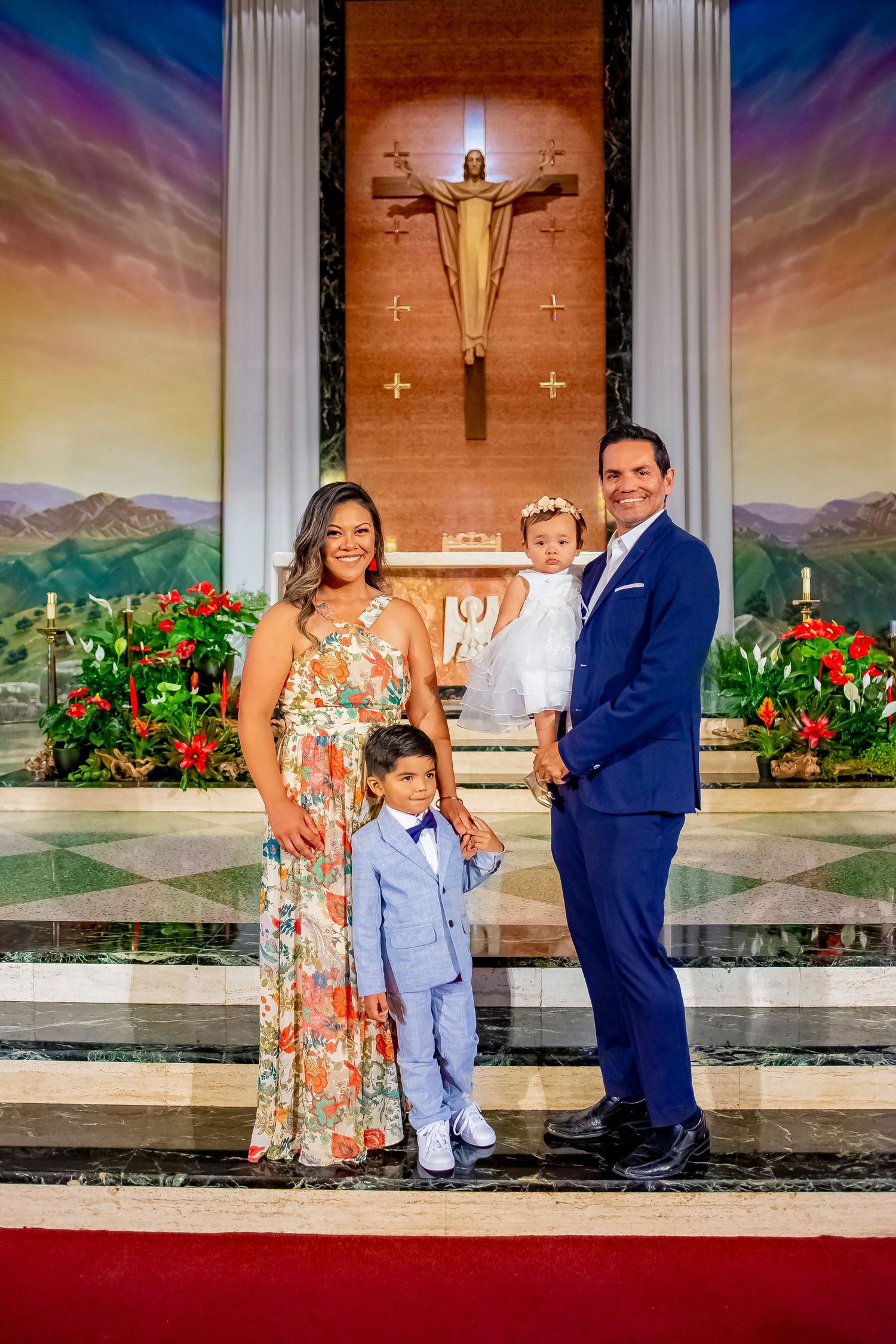 A family poses in front of a church altar with a crucifix and red flowers during a special occasion.