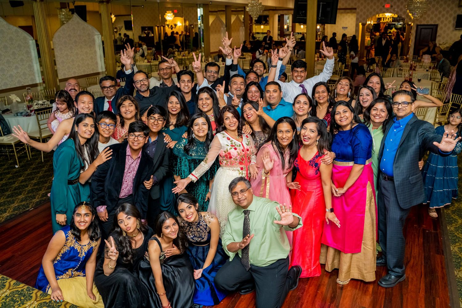 Large group photo of party guests in colorful formal attire at an indoor venue.