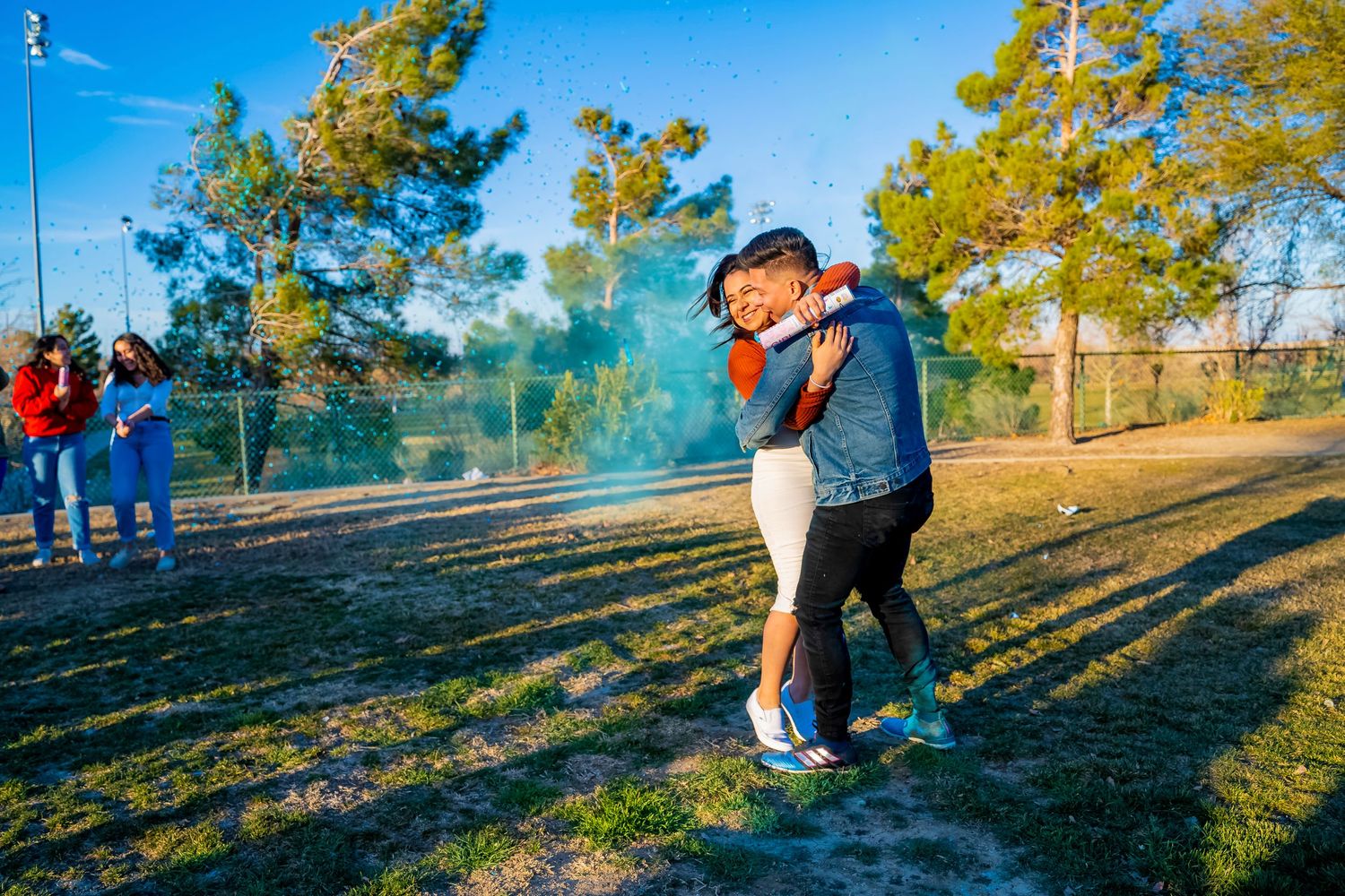 Intimate outdoor moment during a gender reveal celebration with blue smoke.