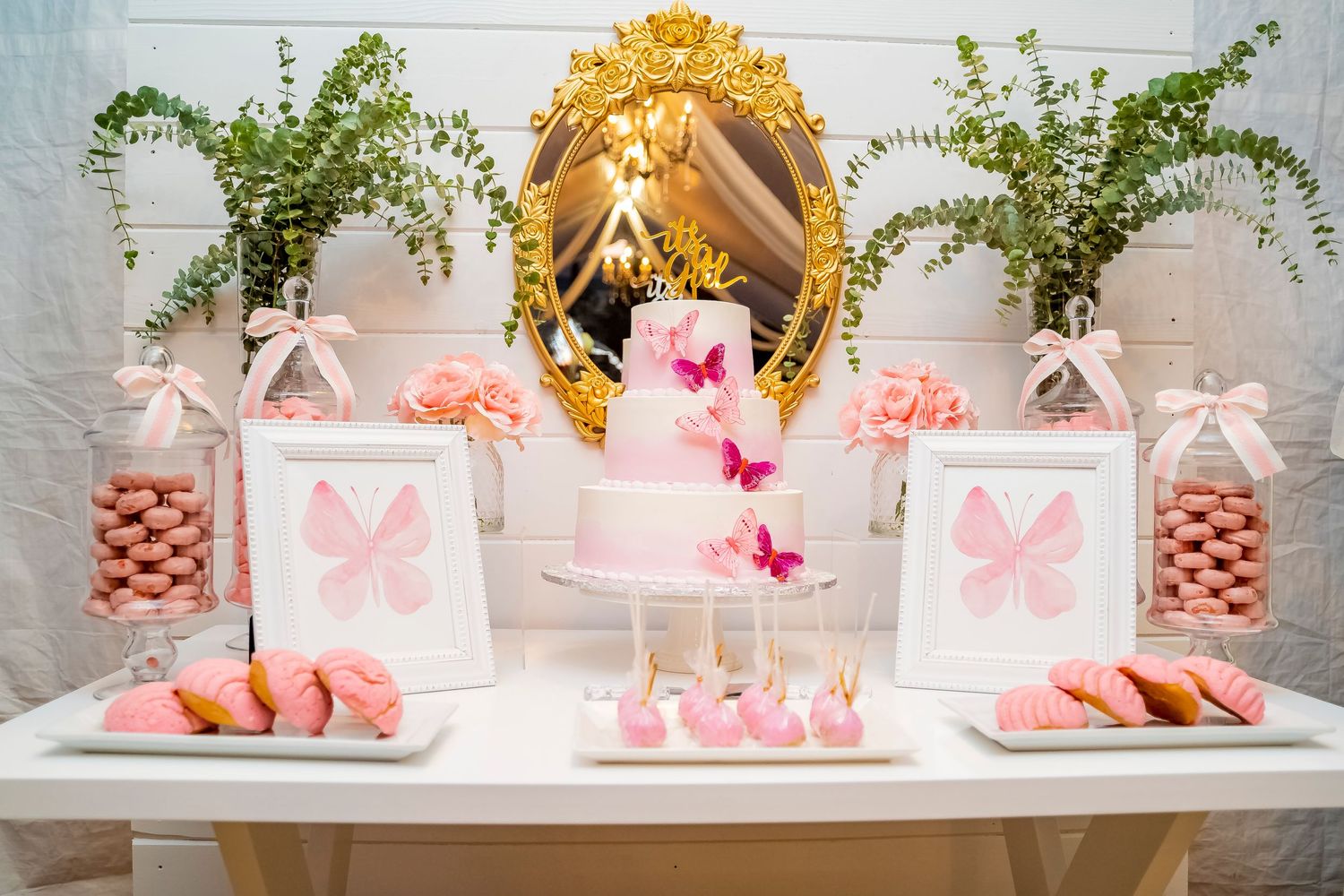 Pink and white themed dessert table with butterfly decorations and floral accents.
