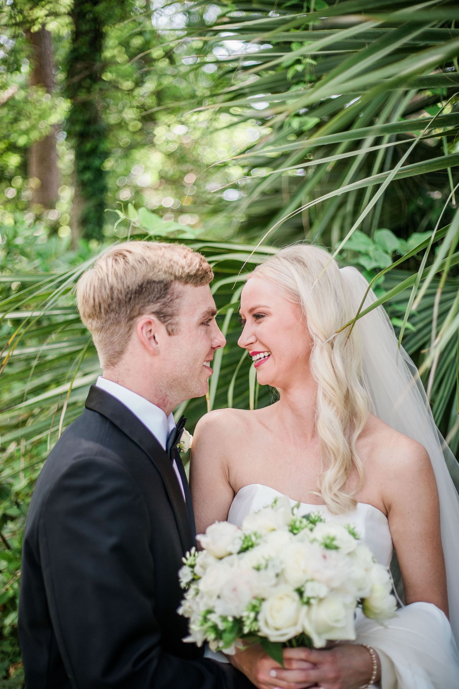 Happy couple shares joyful moment with white bouquet against tropical palm background.